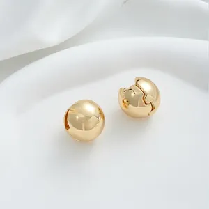 Close-up of polished 14K gold plated sphere huggie earrings on white fabric background