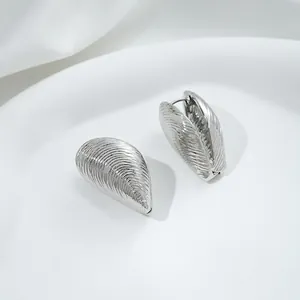 Detailed view of silver shell-textured hoop earrings on a white minimalist display tray