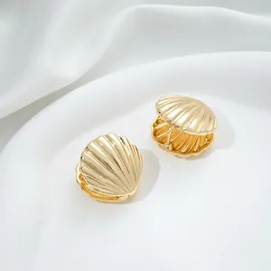Detailed view of 14K gold shell earrings with ribbed texture on white silk fabric