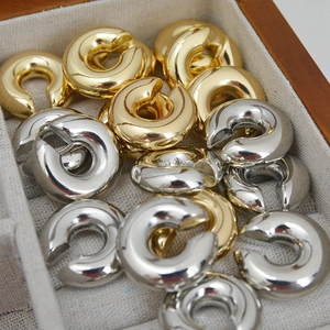Close-up of polished gold and silver C-shaped cuff earrings on a linen jewelry display