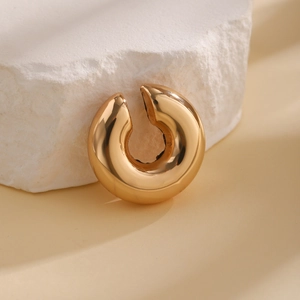 Macro shot of thick gold C-shaped ear cuff on a textured stone with a polished finish