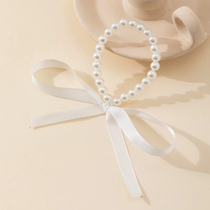 Détail d'un bracelet de perles blanches orné d'un grand nœud en ruban satiné