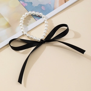 Vue détaillée d'un bracelet en perles blanches orné d'un délicat nœud en ruban noir