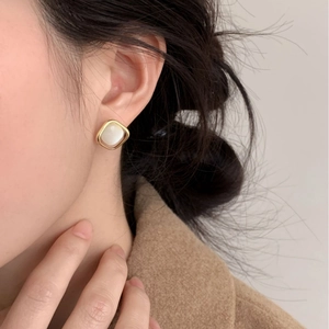 Primer plano de elegantes pendientes cuadrados de opalo lucidos por una modelo con abrigo