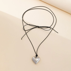 Macro detail of polished heart pendant and black cord bow on a minimalist necklace
