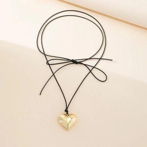 Detail of a shiny gold heart pendant on a thin black cord with a decorative bow knot
