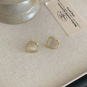 Pendientes minimalistas cuadrados de ojo de gato con marco dorado sobre un fondo de tela beige