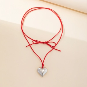 Close-up of a silver heart pendant with red wax cord bow on a minimalist display