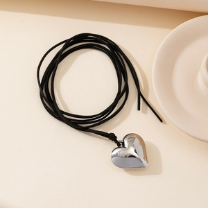 Macro detail of a polished silver heart pendant on a minimalist black velvet cord necklace
