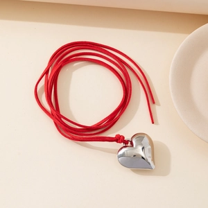 Detailed macro view of a large polished silver heart pendant on a red wax cord necklace