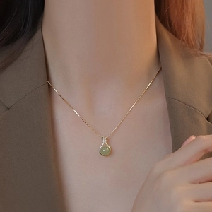 Détail d'un collier doré élégant avec pendentif en jade vert sur un blazer marron
