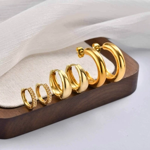 Set di tre paia di orecchini a cerchio dorati con zirconi su espositore in legno