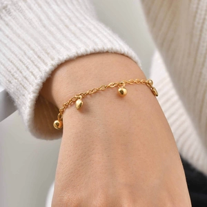 Pulsera dorada con colgantes de corazón y esferas para mujer sobre jersey blanco elegante