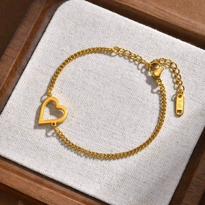 Dettaglio del bracciale a cuore dorato con incisione K18 su sfondo di lino morbido