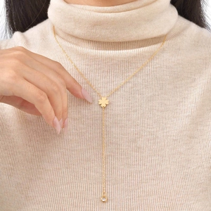 Detail of 18K gold clover pendant necklace with tassel and crystal on a beige sweater