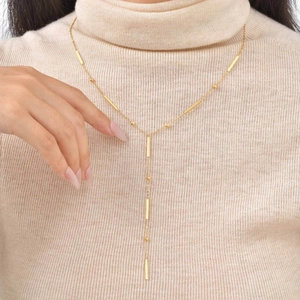 Detail of 18K gold Y-necklace with imitation pearls and tassel on beige sweater