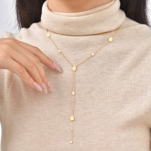 Detail of a gold 18K Y-shaped tassel necklace with water drop charms on beige sweater