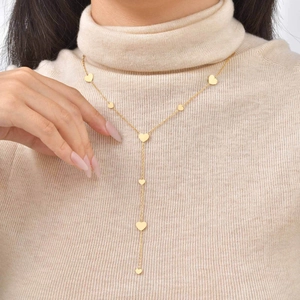 Golden heart tassel Y-necklace for women worn over a beige turtleneck sweater