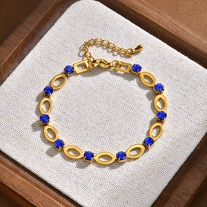 Detail of gold chain bracelet with hollow oval links and round blue gemstones on texture