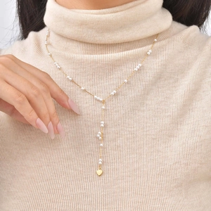 Detail of 18K gold Y-necklace with delicate white pearls and heart tassel pendant