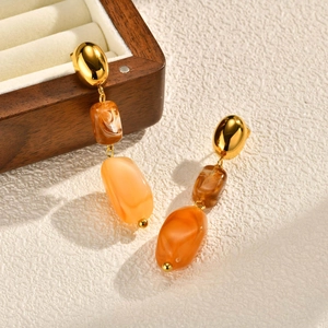 Close-up of amber resin drop earrings with golden metallic studs and artistic texture