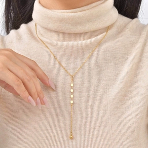 Detail of 18K gold Y-necklace with metallic discs and imitation pearls on beige sweater