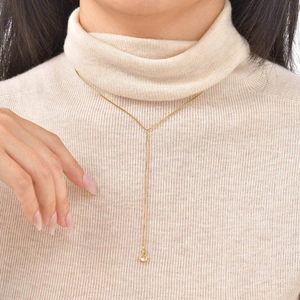 Detail view of 18K gold Y-shaped necklace with flower pearl and tassel on a beige sweater