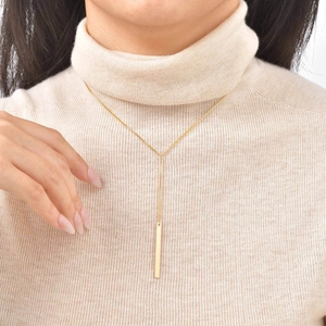 Detail of 18K gold Y-necklace with bar pendant worn on a beige knit sweater