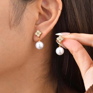 Gros plan détaillé de boucles d'oreilles trèfle dorées avec perles sur un mannequin