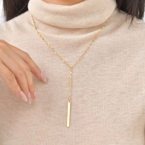 Detail of 18K gold-plated Y-shaped necklace with tassel on beige knit sweater