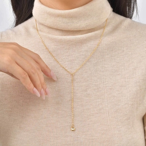 Detail of 18K gold Y-necklace with flower pearl and crystal pendant on beige sweater