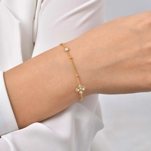 Détail d'un bracelet trèfle doré avec zircons porté au poignet sur manche blanche