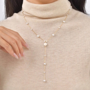 Detail of 18K gold Y-necklace with daisy pendant and pearls on khaki sweater