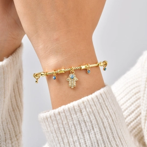 Detailed view of a gold Hamsa Hand and Evil Eye charm bracelet on a model's wrist