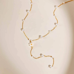 Elegant gold Y-shaped flower necklace with white pearls on a minimalist background