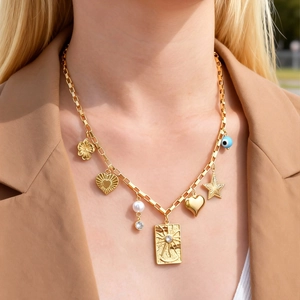 Détail d'un collier bohème doré avec charms cœur, étoile et œil porté par un mannequin