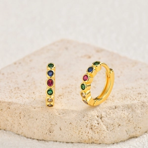 Detail of gold hoop earrings with multi-colored round zircons on a textured stone base