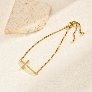 Detailed view of adjustable gold cross bracelet with shimmering pave stones and bead clasp