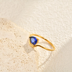 Detail view of a pear-cut blue zircon gold ring with an elegant wave-shaped band design