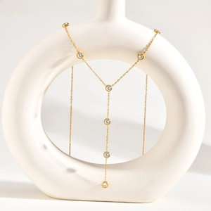 Dettaglio della collana a Y dorata con cristalli rotondi su un vaso di ceramica bianco