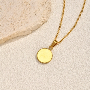 Gros plan du collier disque rond en acier doré sur fond de travertin naturel