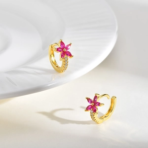Détail de boucles d'oreilles fleurs dorées avec zircons roses sur une assiette blanche