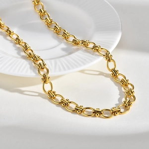Detail of golden stainless steel link chain necklace on a minimalist white ceramic plate