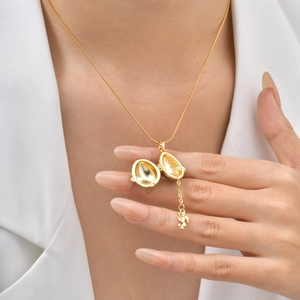 Détail macro du médaillon œuf doré s'ouvrant sur un petit pendentif ange élégant