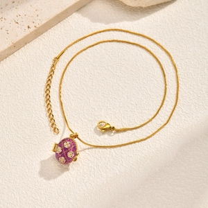 Détail d'un pendentif œuf en émail violet avec motifs en losange dorés sur chaîne