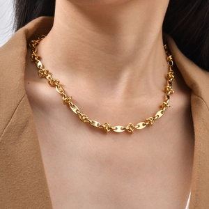 Close-up of a gold stainless steel chain link necklace on a model wearing a camel blazer