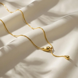 Elegante gouden roestvrijstalen Y-ketting met druppelhanger op zijden achtergrond