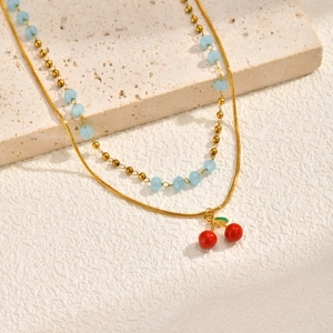 Collana a doppio strato dorata con perle azzurre e un ciondolo a forma di ciliegia rossa