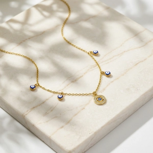 Detalle de collar ojo turco dorado con colgantes de esmalte azul sobre fondo mármol