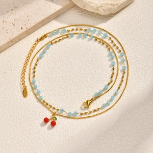 Dettaglio della collana a doppio strato dorata con perline blu e pendente ciliegia